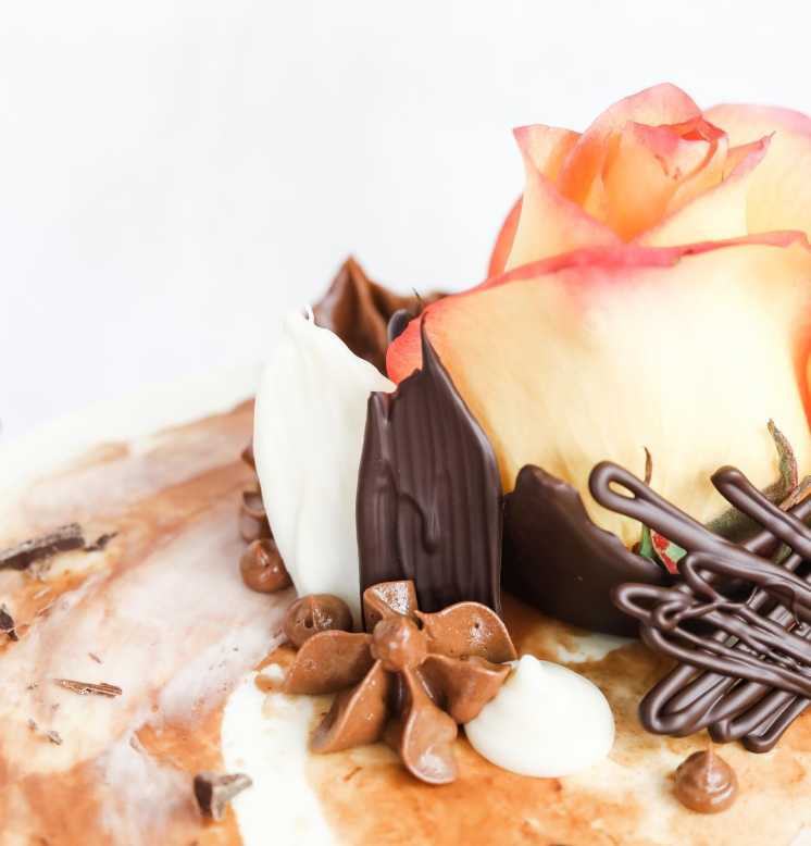 Close-up of chocolate shards, piped ganache rosettes and a fresh rose